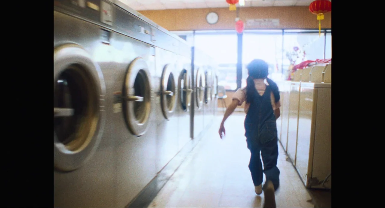 Everything Everywhere All At Once (2022) movie still: fullbody — A row of industrial-sized metal dryers lines the side of a sunlit community…
