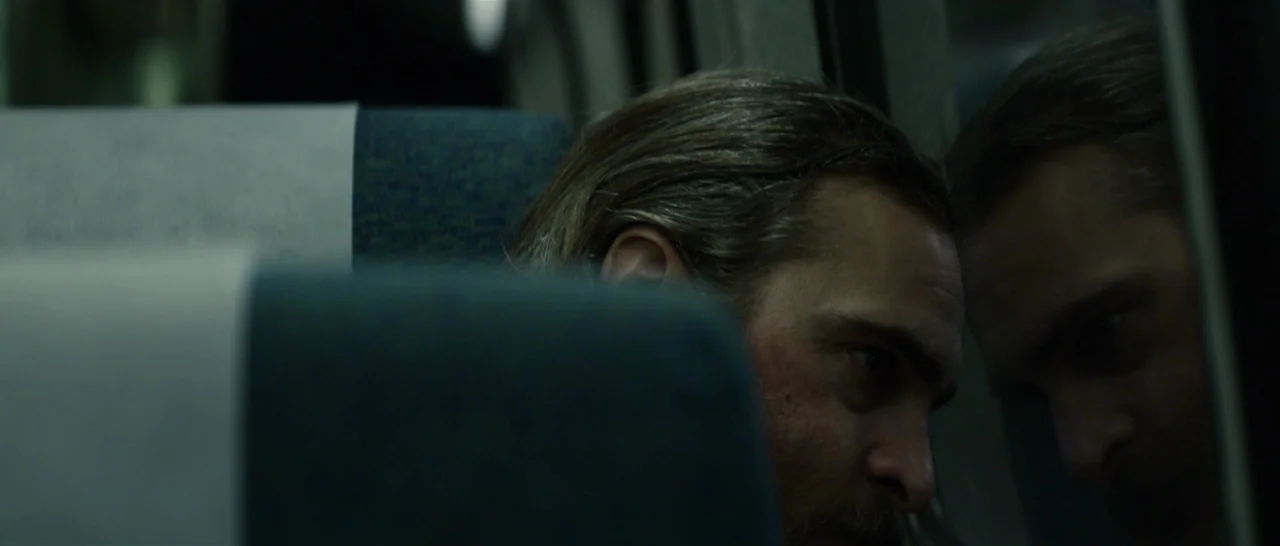 You Were Never Really Here (2017) movie still: closeup — A dark, dimly lit train carriage interior with blue upholstered seats and window glass. A…