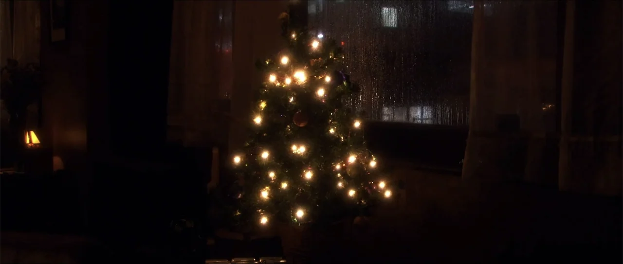 El acto (1989) movie still: medium — A living room interior at night with a decorated christmas tree in the center. The tree is lit with small…