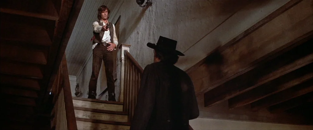 Pat Garrett & Billy The Kid (1973) movie still: wide — A wooden staircase in a dimly lit 19th-century building with rough, plastered walls. A man…