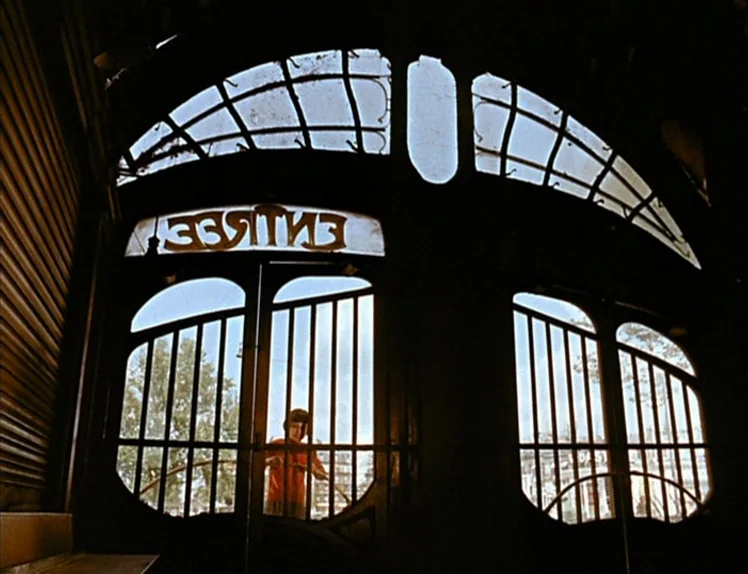 Zazie Dans Le Métro (1960) movie still: wide — An interior shot looking out through an Art Nouveau metal gate labeled ENTRÉE. A young person in an…
