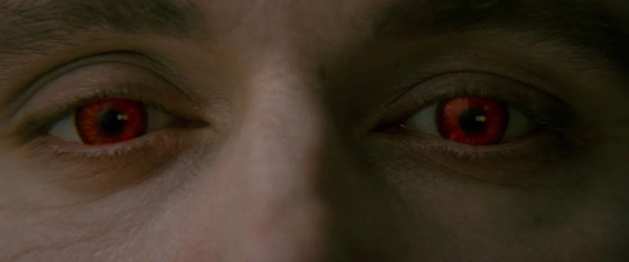 The Twilight Saga: New Moon (2009) movie still: closeup — A close-up view focuses on a pair of human eyes with distinct red irises. The skin around…