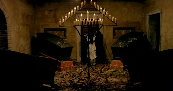 Blood For Dracula (1974) movie still: wide — An underground stone chamber contains two dark caskets and dead leaves covering the floor. Three…