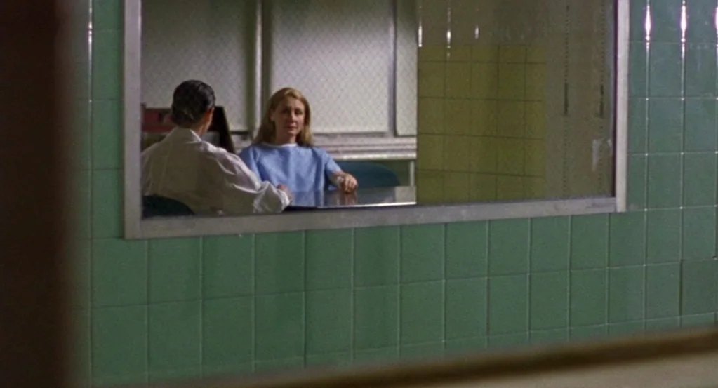 The Station Agent (2003) movie still: medium — A clinical room features green square tiles and a large observation window with wire glass. A woman…