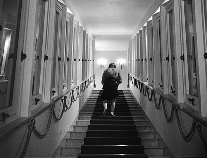 Nights of Cabiria (1957) movie still: fullbody — A symmetrical stone staircase leads upward between two long walls lined with numerous windows. A…