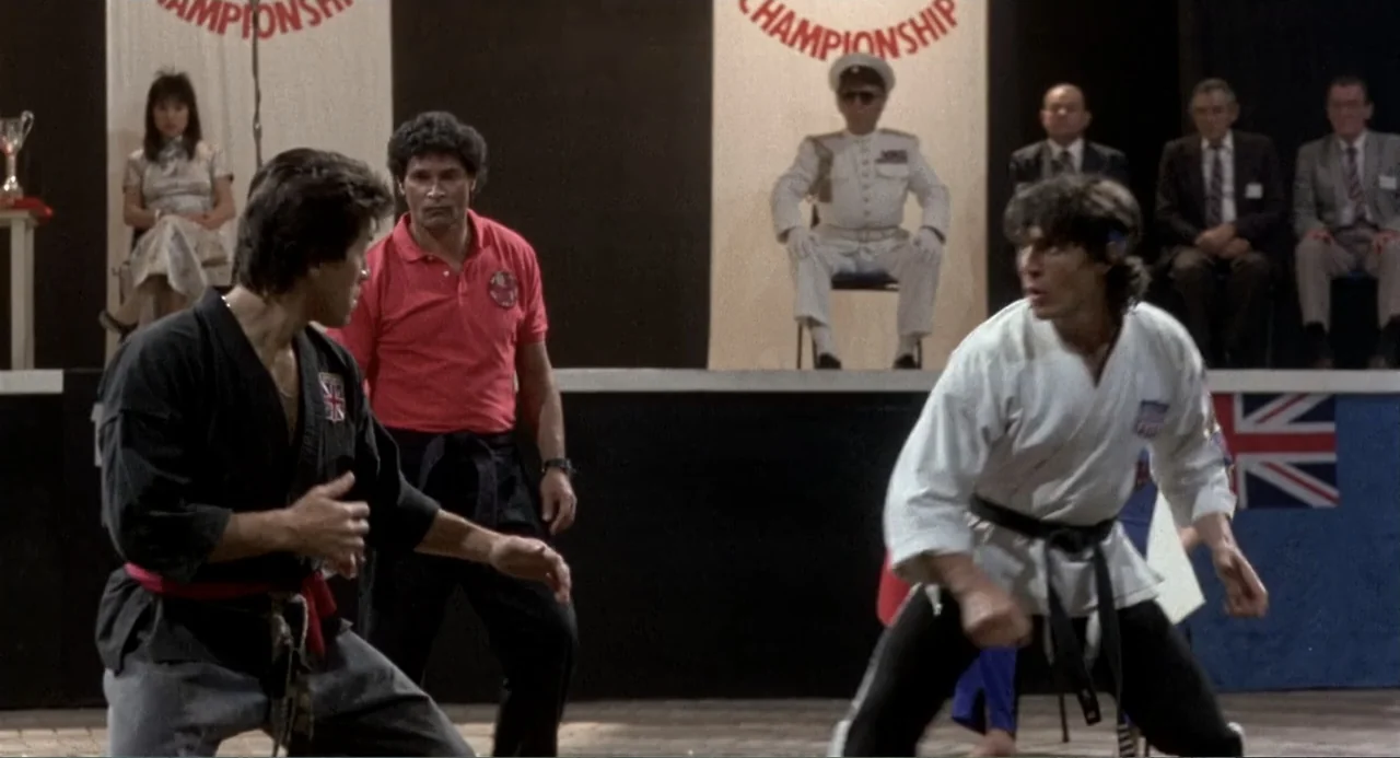 American Ninja 3: Blood Hunt (1989) movie still: medium — A gymnasium interior features a competition platform with spectators and judges in the…