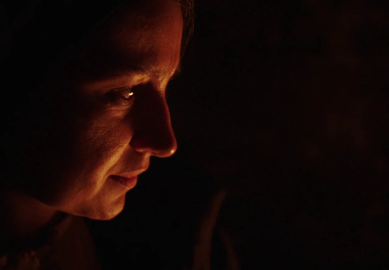 You Won’t Be Alone (2022) movie still: closeup — A dark environment with a single subject visible only on one side of frame. The woman's face is…