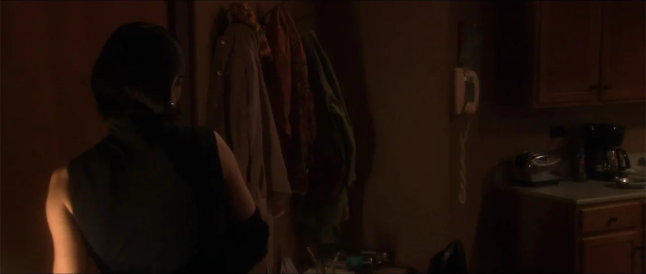 El acto (1989) movie still: medium — A dimly lit interior apartment setting features cabinets and coats hanging on a wall. A woman in a sleeveless…