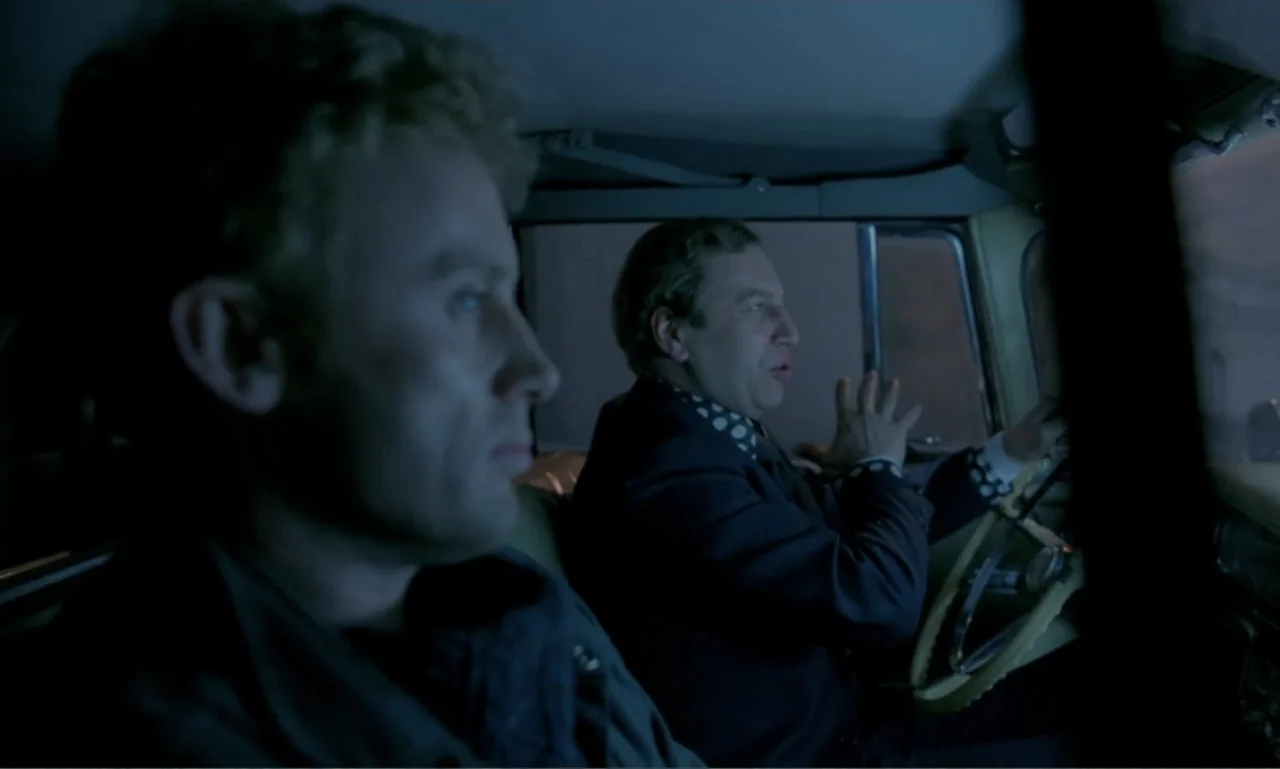 Ga-ga: Glory to the Heroes (1986) movie still: medium — The interior of a vintage car at night contains two men in conversation. The driver gestures…
