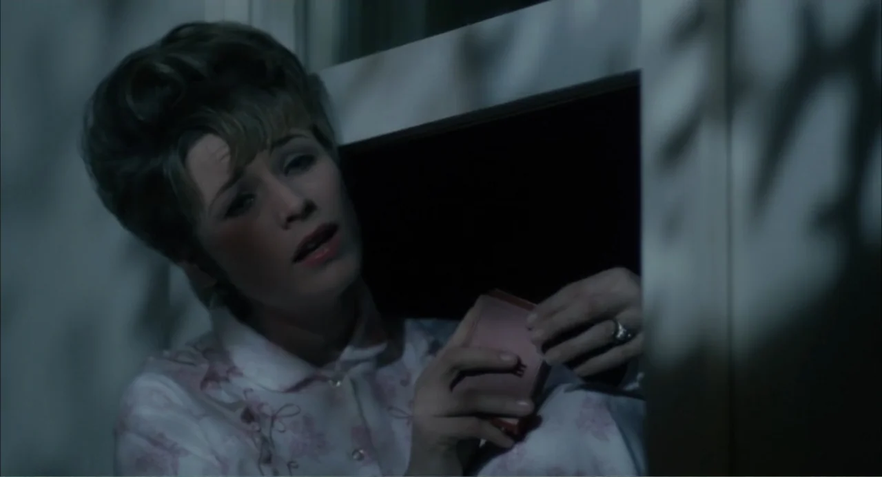 Cottonpickin' Chickenpickers (1967) movie still: closeup — A dimly lit room features a woman positioned near a paneled window frame. She holds a…