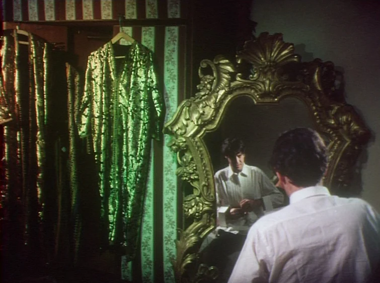 Hermitage (1968) movie still: medium — A dressing room features vertical striped wallpaper and several hanging metallic green robes. A man stands…