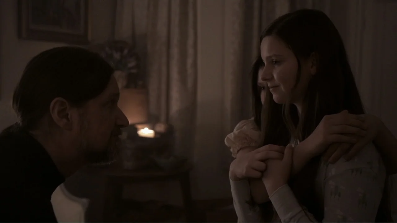 Paranormal Activity: The Ghost Dimension (2015) movie still: medium — A dimly lit room with draped curtains visible in the background behind a…