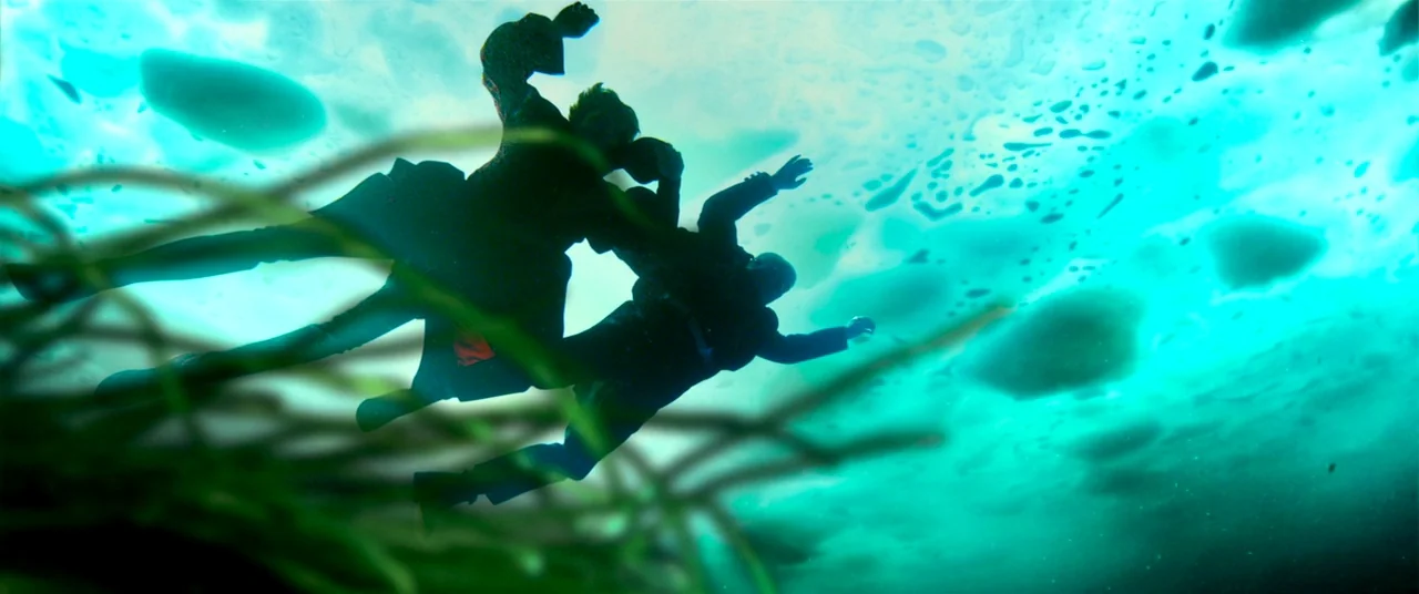 The House That Jack Built (2018) movie still: wide — Two figures are suspended in a bright turquoise underwater environment with floating debris.…