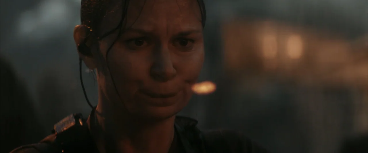 The Tomorrow War (2021) movie still: closeup — An outdoor battlefield at night is filled with dark, indistinct shapes and atmospheric smoke. A woman…