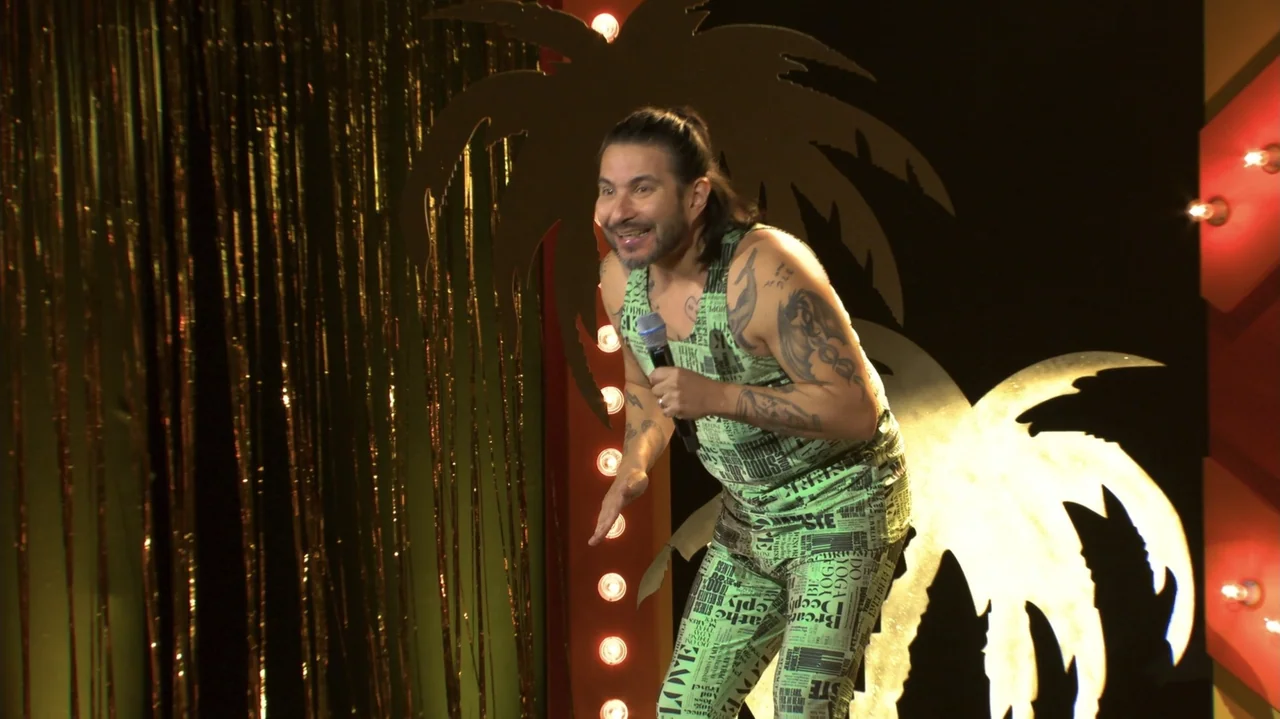 Felipe Avello: Doglover (2024) movie still: medium — A man stands on a stage in front of a golden fringe curtain. He wears a matching green tank top…