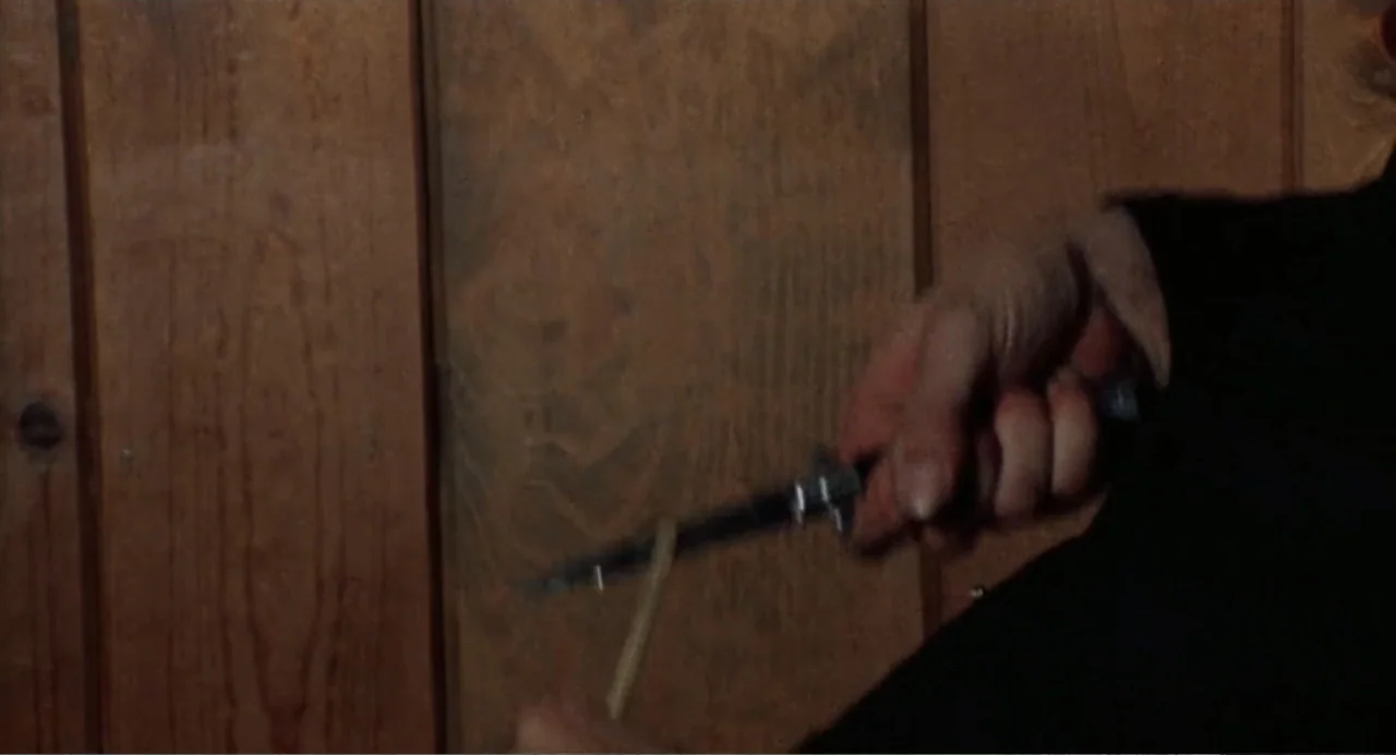 The Last House on the Left (2009) movie still: closeup — Vertical wooden panels serve as the background for a close encounter with a weapon. A hand…