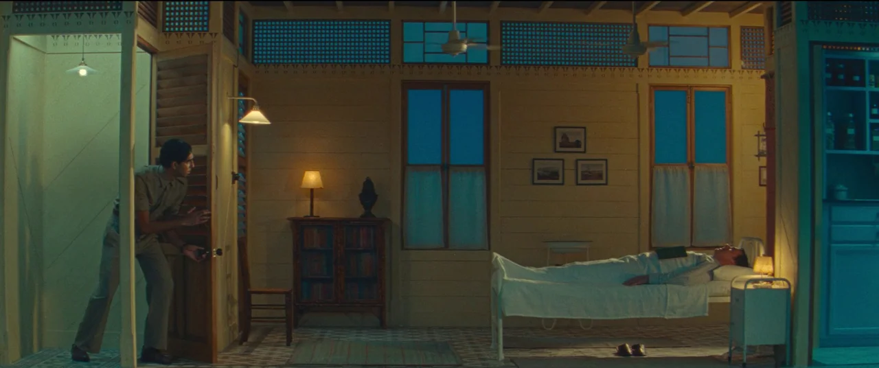Poison movie still: wide — A symmetrically composed hospital room features a patient resting in bed under dimmed lighting. A man stands in an…