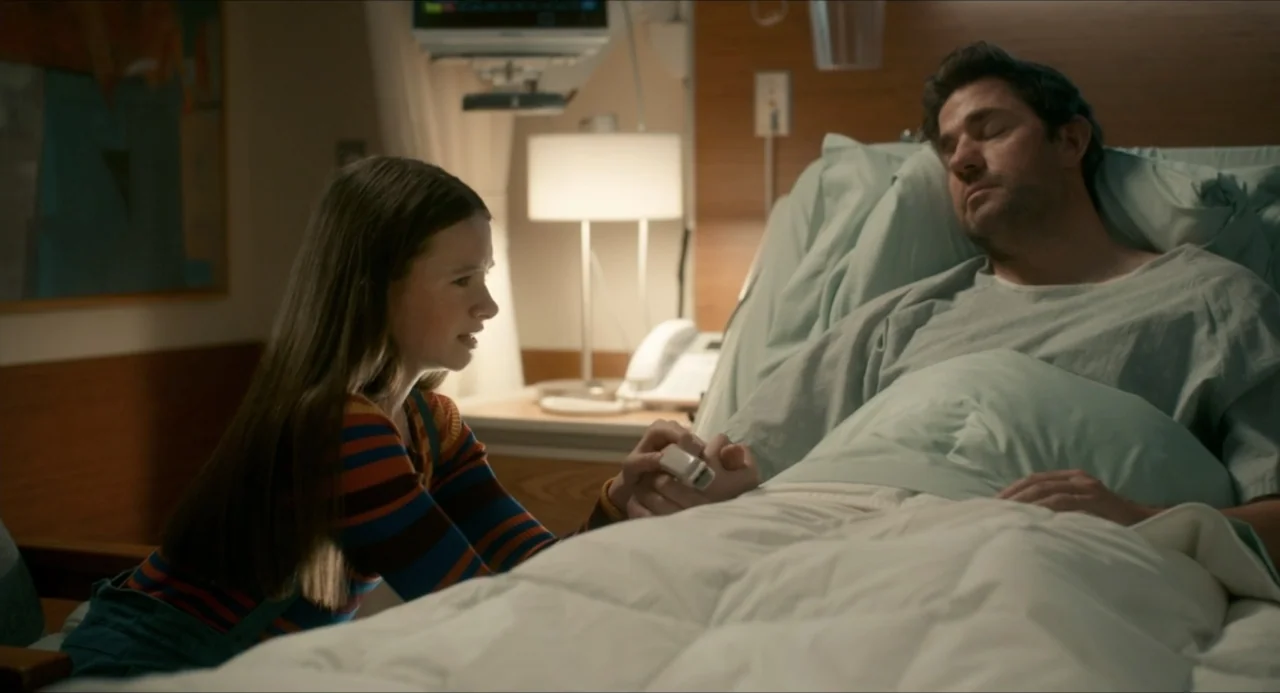 IF (2024) movie still: medium — A modern hospital room features wood-paneled walls and a clinical bed with white linens. A teenage girl sits beside…