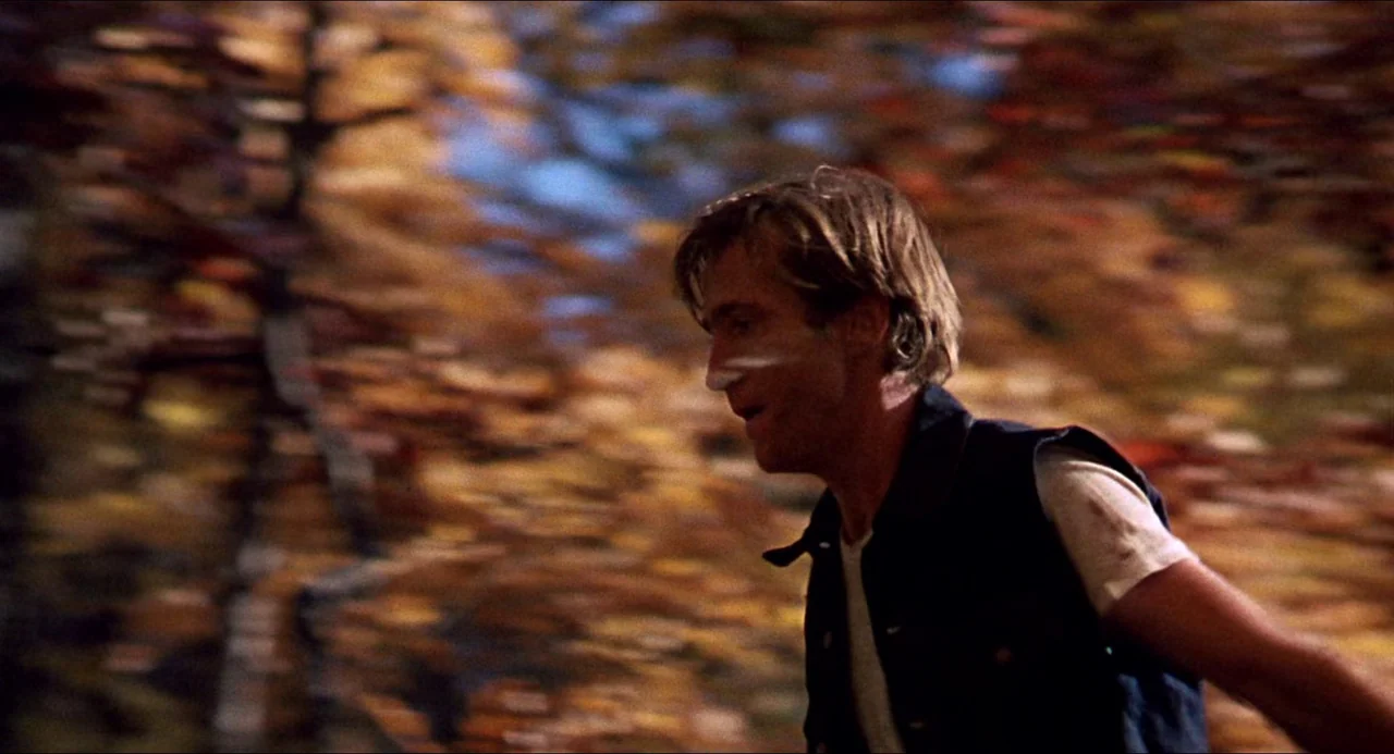 In the Heat of the Night (1967) movie still: medium — A man moves quickly through a dense area filled with autumn foliage. The out-of-focus orange…