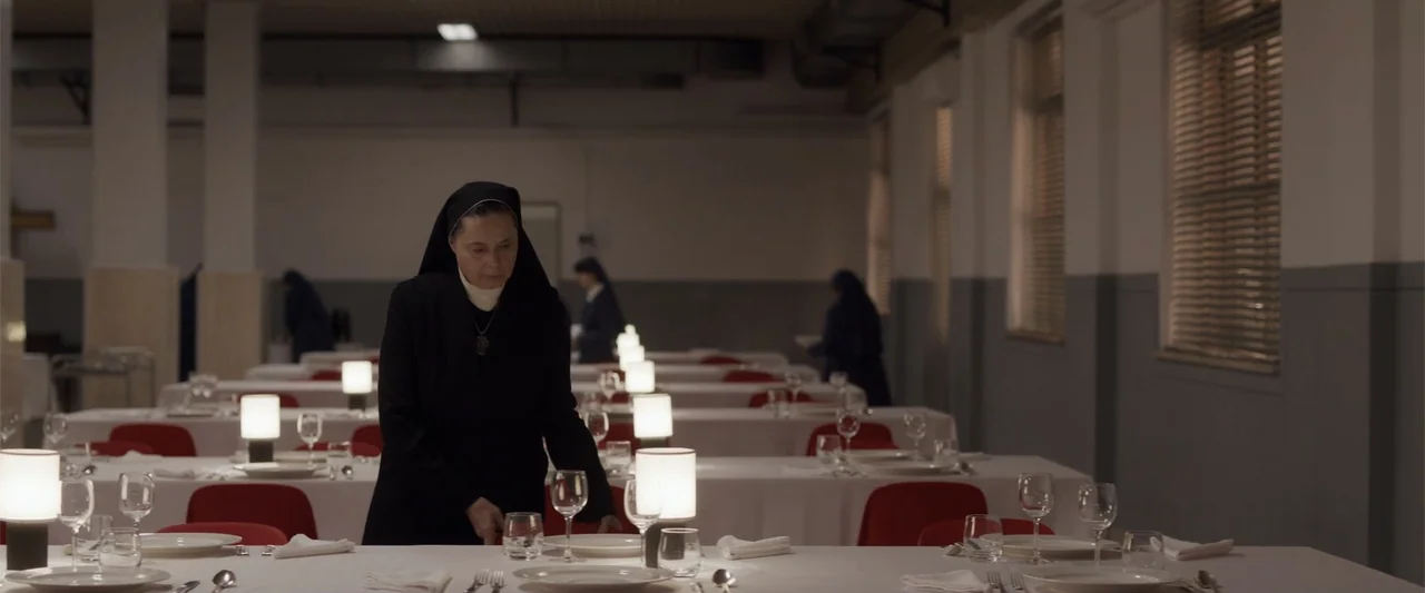Conclave (2024) movie still: medium — A spacious dining hall features multiple rows of tables covered in clean white linens. A woman wearing a black…