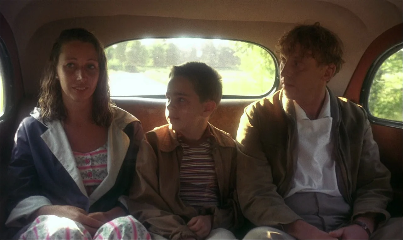 My Life As A Dog (1985) movie still: medium — The interior of a vintage car features three people seated across the back row. A woman, a young boy,…