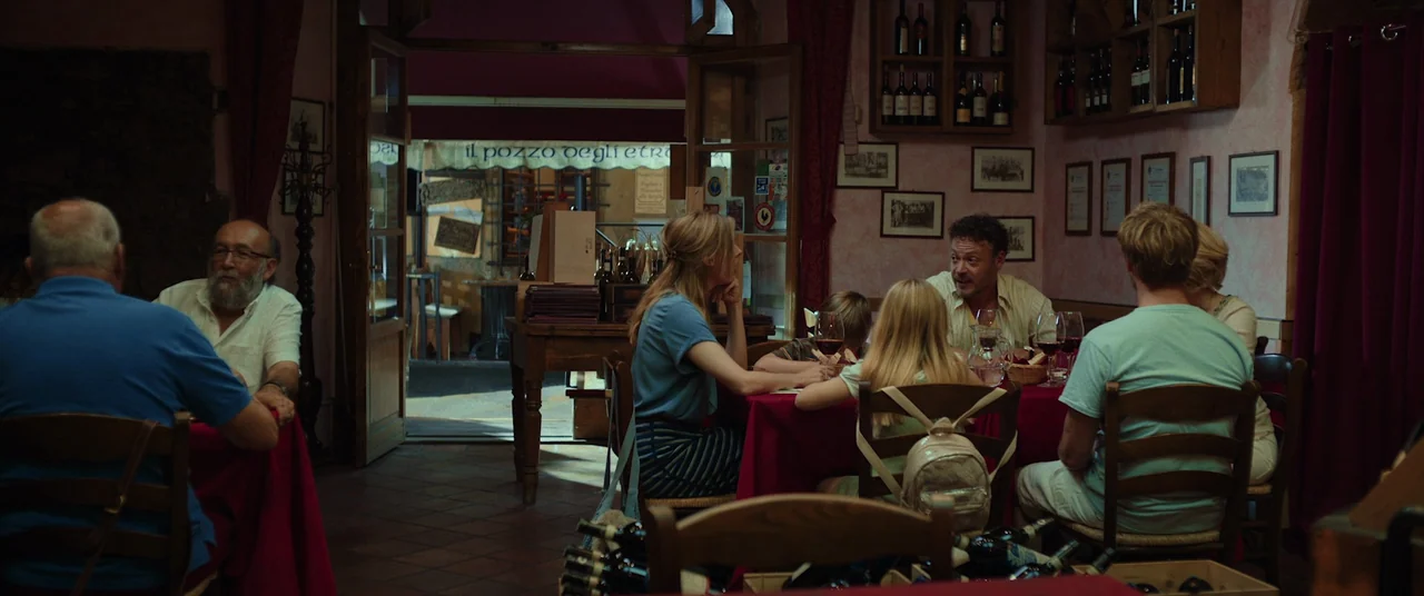 Speak No Evil (2022) movie still: wide — An Italian trattoria interior with rustic wooden furniture and framed photographs on pink walls. Several…