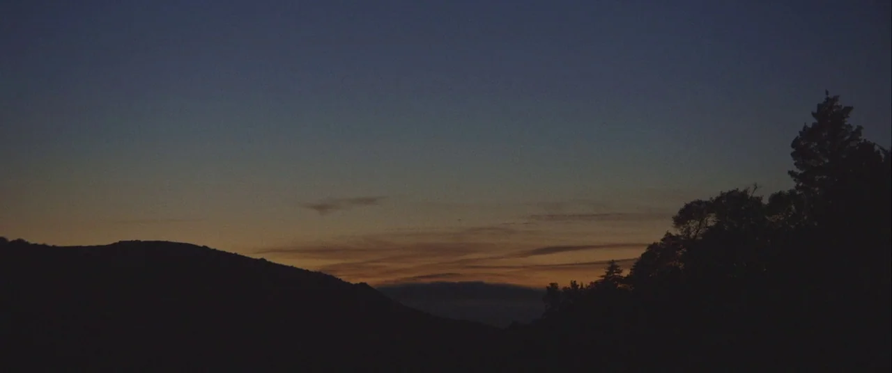 Always Shine (2016) movie still: establishing — A dark mountainous silhouette stretches across the bottom of a twilight sky. Wispy clouds are…