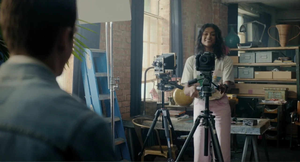 Picture This (2008) movie still: medium — A workshop space features brick walls, wooden shelving units, and various photography equipment pieces. A…