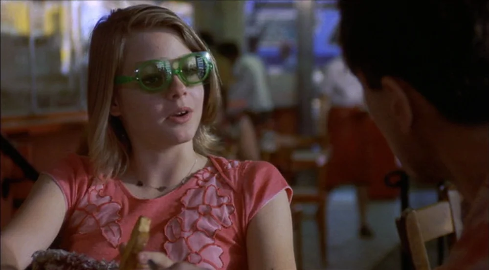 Taxi Driver (1976) movie still: medium — A diner interior with blurred tables and chairs in the background. A young woman wearing bright green…