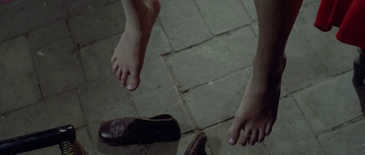 What Have They Done To Your Daughters? (1974) movie still: closeup — A pair of bare legs dangle above a grey stone-paved floor. A single brown…