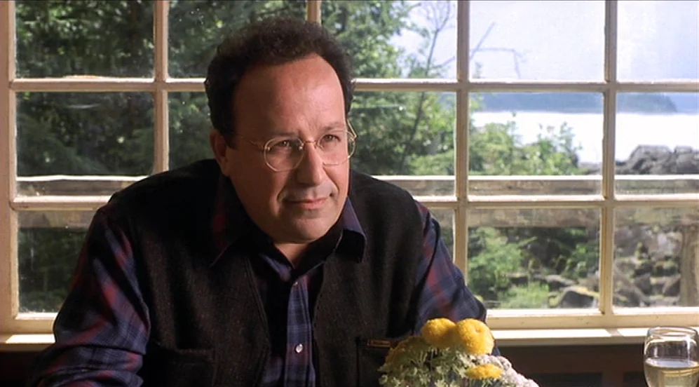 Limbo (1999) movie still: medium — A man sits at a table in front of a window overlooking a landscape. Bright daylight streams through the window…