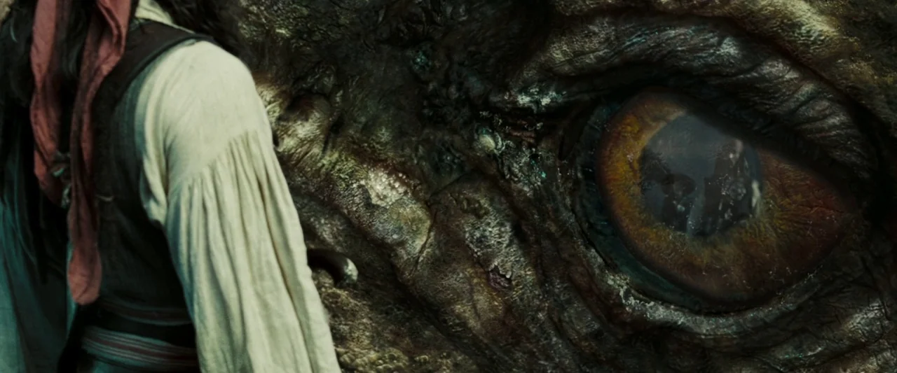 Pirates of the Caribbean: At World’s End movie still: closeup — A dark, textured environment featuring the massive, weathered eye of a mythical…
