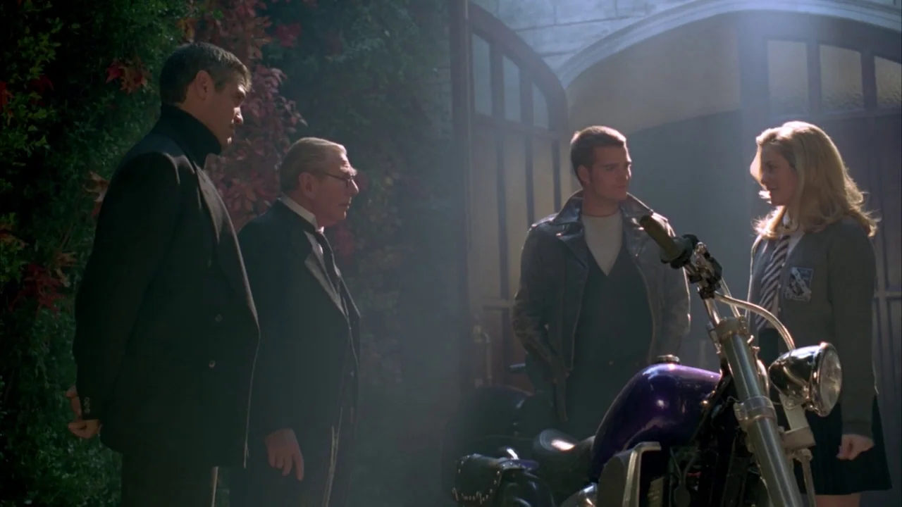 Batman & Robin (1997) movie still: wide — A stone courtyard features a large wooden double door covered in climbing ivy vines. Four people stand in…