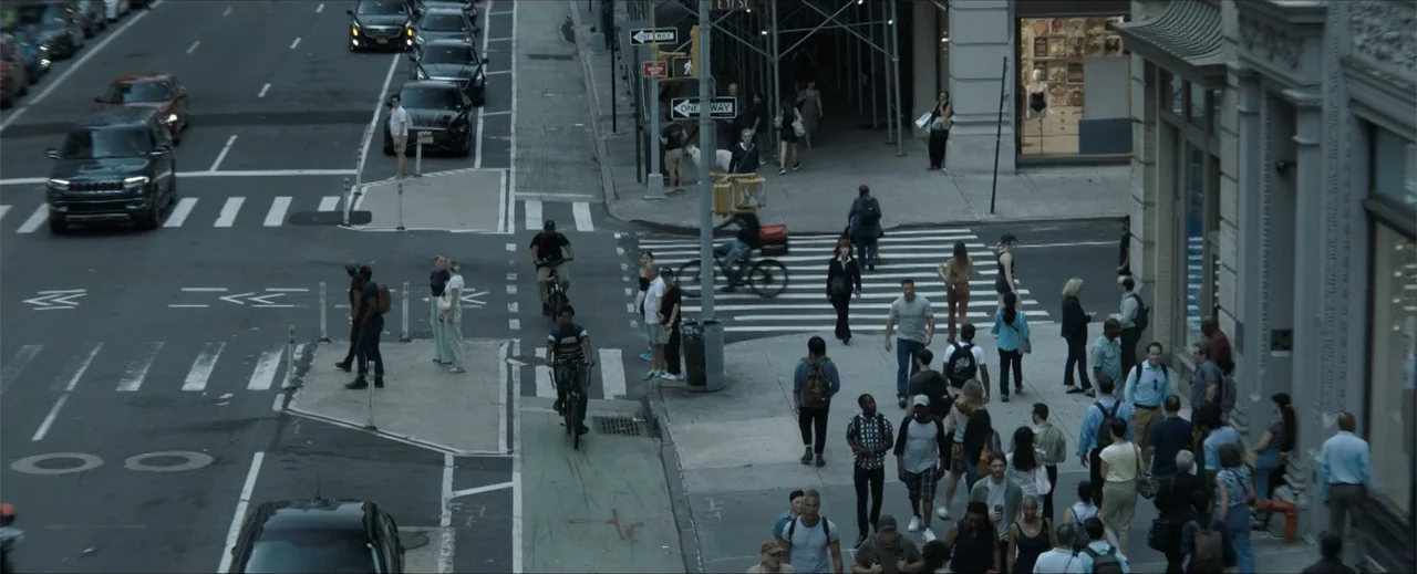 Venom: The Last Dance (2024) movie still: wide — A dense urban intersection with pedestrians, cyclists, and vehicles crossing at a busy corner.…