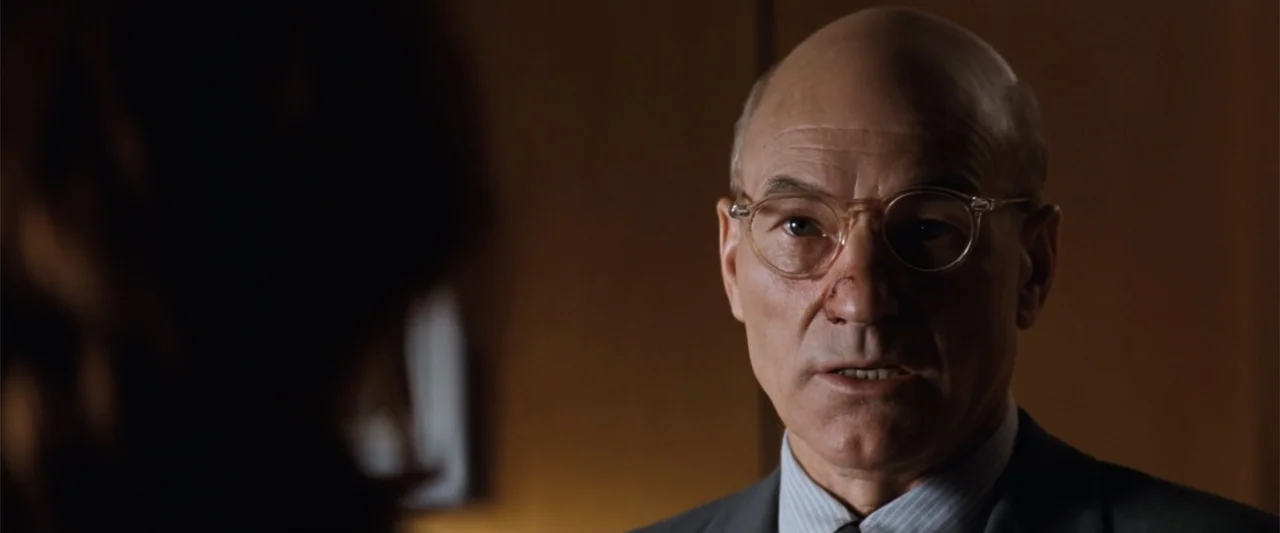 Conspiracy Theory (1997) movie still: closeup — A dark office features a wood-paneled wall in the background. An older man in a grey suit and…