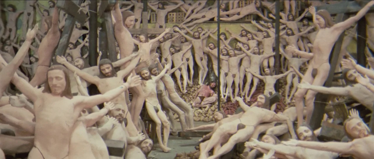 The Holy Mountain (1973) movie still: wide — A cluttered storage room contains a large mass of identical wooden crucifix figures. The statues stand…