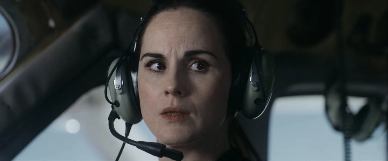 Flight Risk (2025) movie still: closeup — A close view inside a helicopter cockpit with visible structural glass and metal panels. A woman wearing…