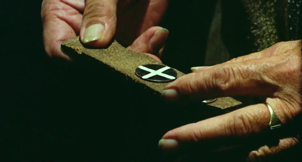 Wake In Fright (1971) movie still: closeup — A dark environment frames a person's aged hands holding a textured leather strap. A circular metal…