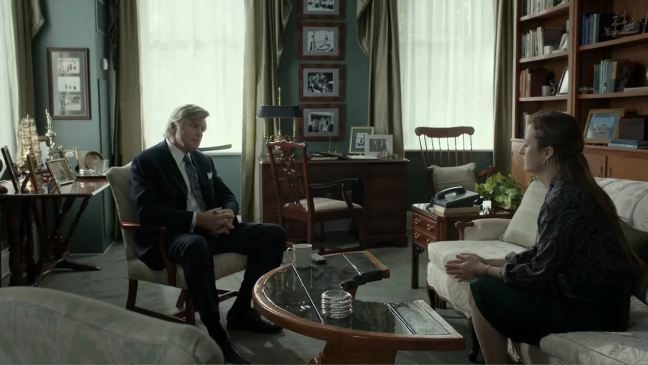 Confirmation (2016) movie still: medium — A well-furnished room featuring wooden bookshelves, framed pictures, and multiple upholstered chairs. An…