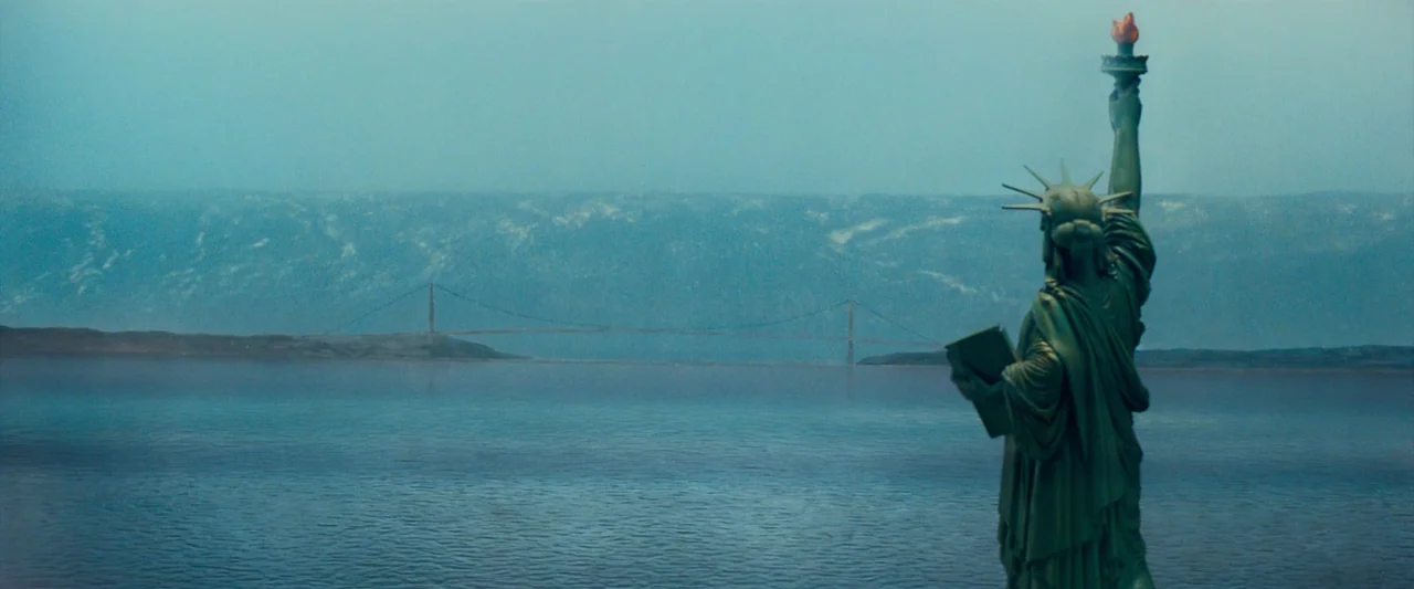 The Abyss (1989) movie still: wide — A view across a large, calm body of water with a distant suspension bridge. The Statue of Liberty stands in the…
