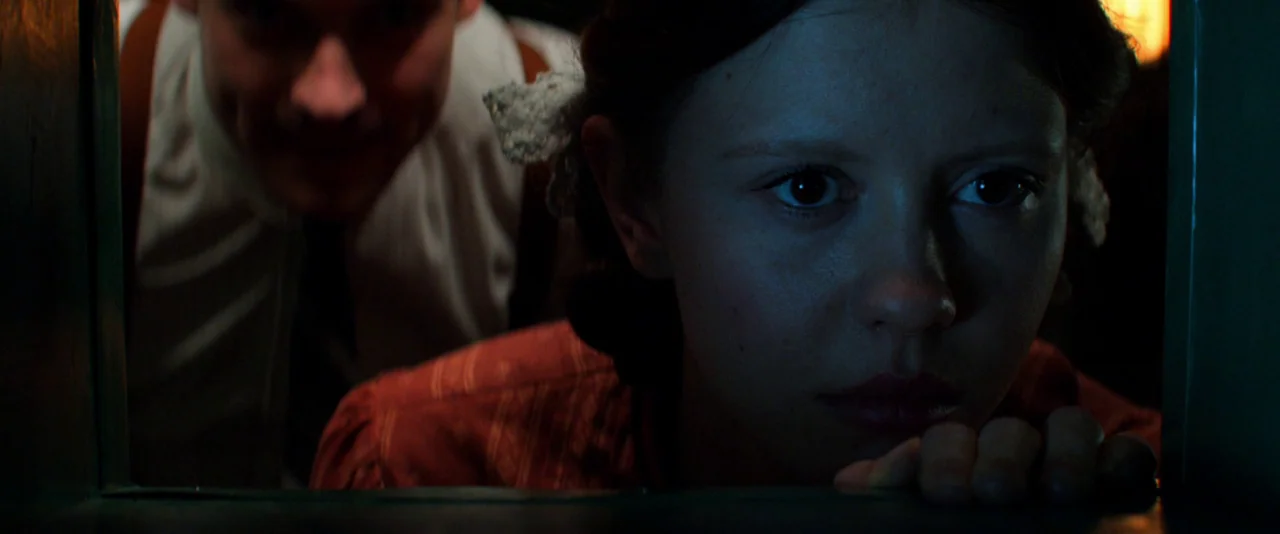 Pearl (2022) movie still: closeup — The dark interior setting appears to be a damp, enclosed basement or cellar space. A young woman looks ahead…