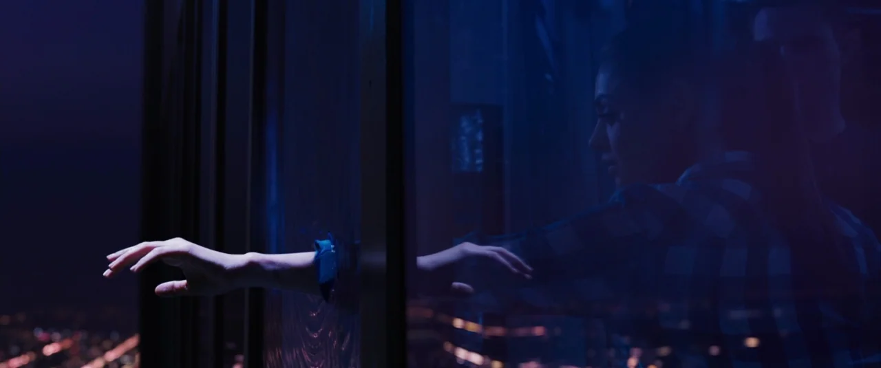 Jupiter Ascending (2015) movie still: medium — A dark room overlooks a blurred city grid lit by distant night lights. A woman faces the window and…