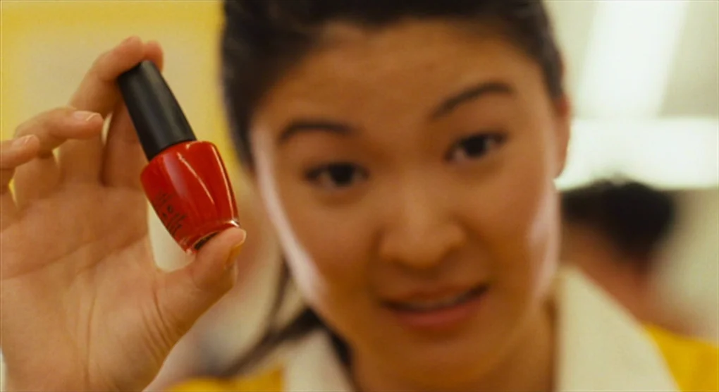 The Savages (2007) movie still: closeup — A woman stands in a bright room with yellow walls and fluorescent lighting. She holds up a small bottle of…