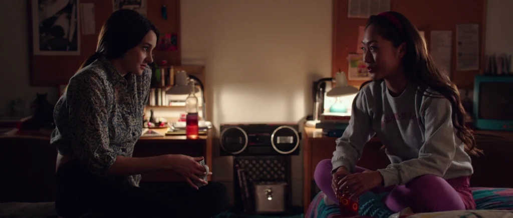 White Bird in a Blizzard (2014) movie still: medium — A dorm room contains two young women sitting on a bed between two desks. A vintage boombox…