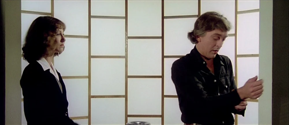 Deep Red (1975) movie still: medium — A man and woman stand before a shoji-style paper partition wall. The man adjusts his cuff while the woman…