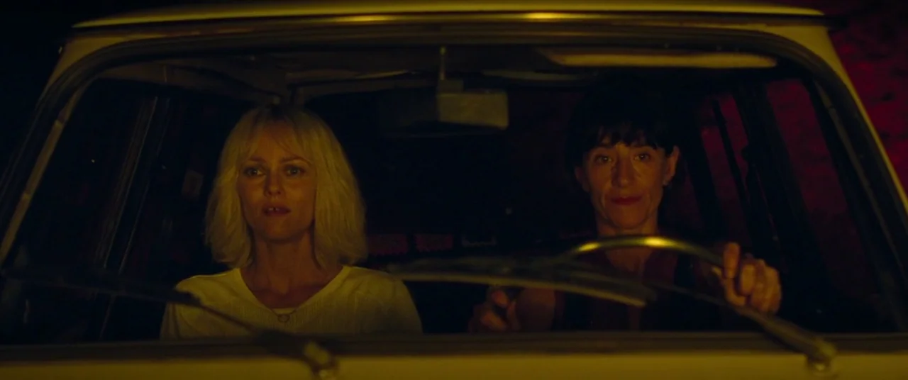 Knife+Heart (2018) movie still: medium — Two women sit in the front seats of a car during the night. The vehicle interior is dark, illuminated by a…