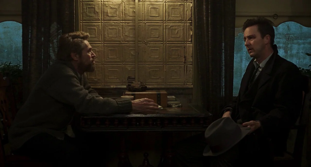 Motherless Brooklyn (2019) movie still: medium — A dimly lit train car features dark wood paneling and aged metallic wall accents. Two men sit…