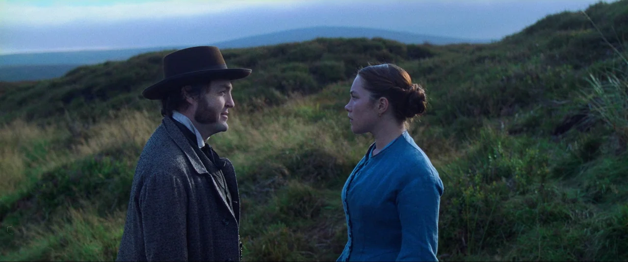 The Wonder (2022) movie still: medium — A desolate, grassy moorland with rolling hills stretches into the horizon during evening. A man in a wool…