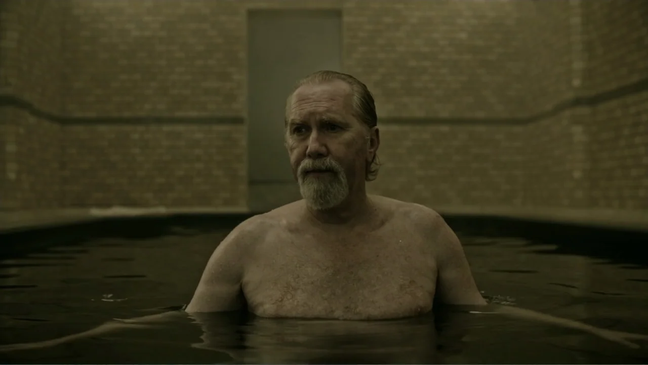 A Cure for Wellness (2017) movie still: medium — A dimly lit indoor swimming pool with bare brick walls and dark water. A middle-aged man stands…