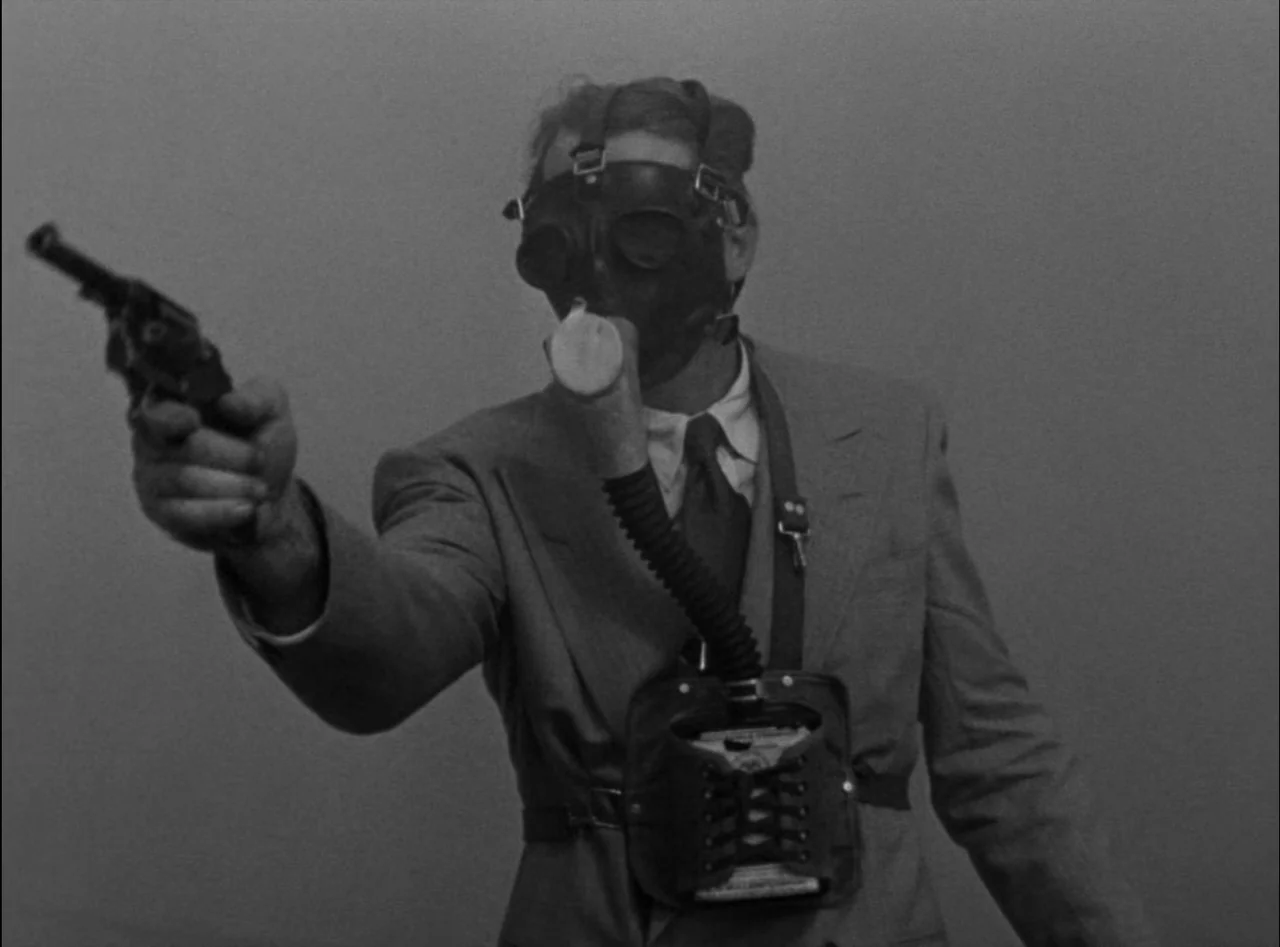 Criss Cross (1949) movie still: medium — A featureless, grey background provides no context for the location. A man wears a gas mask and suit while…